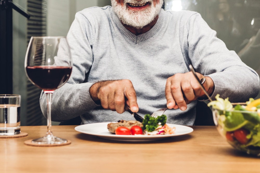 Happy,Senior,Man,Eating,Pork,Steak,On,Table,At,Restaurant