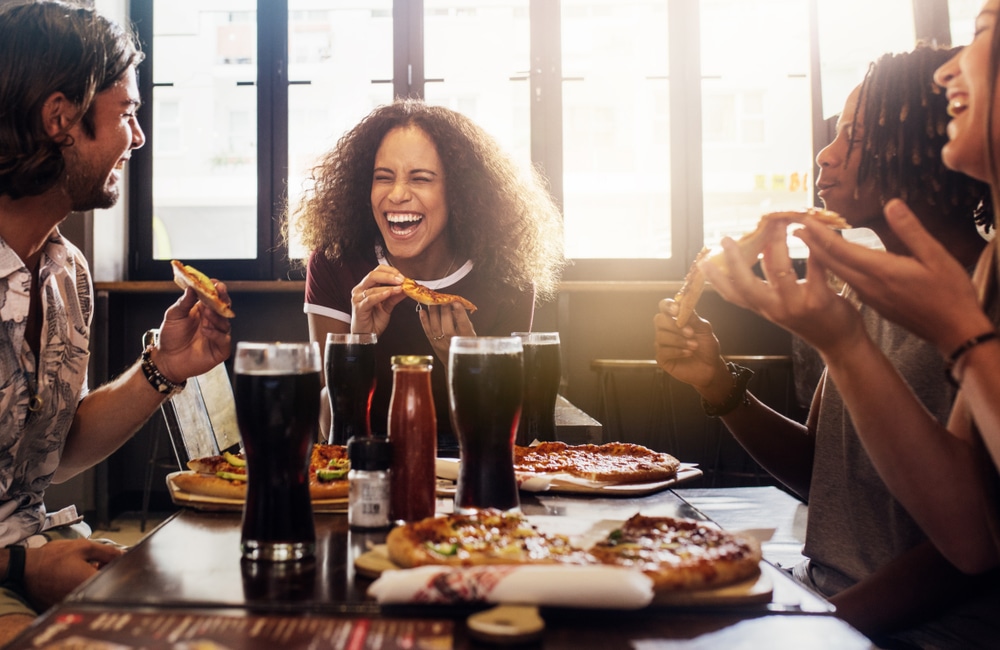 Young,Woman,Eating,Pizza,And,Laughing,While,Sitting,With,Her