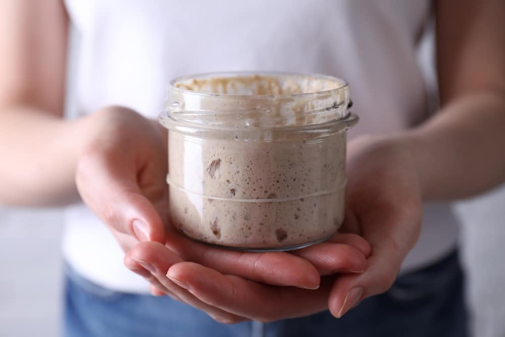Woman,Holding,Glass,Jar,With,Fresh,Sourdough,Starter,,Closeup